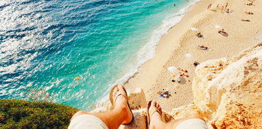 Feet hanging over a rock with a view of the beach and sea below.