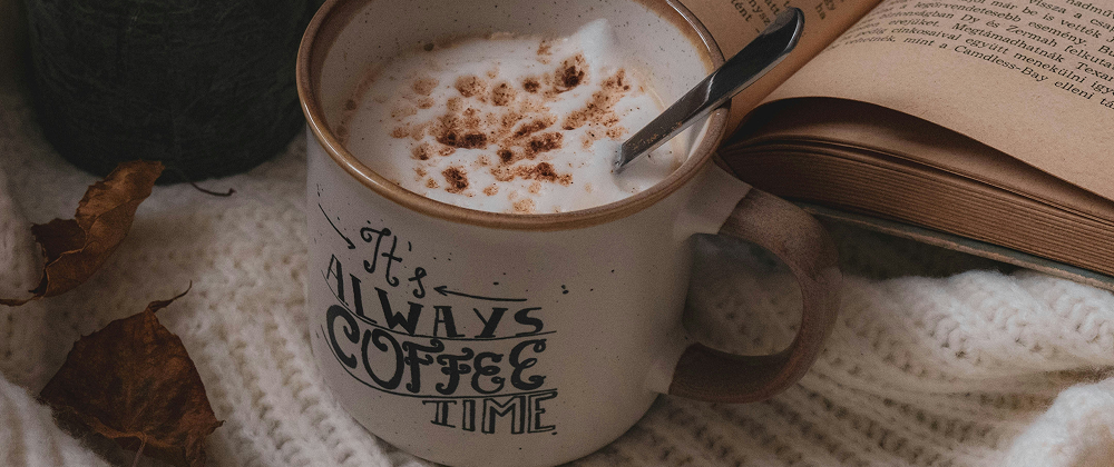 Mug of frothy coffee with cinnamon beside an open book on a cosy white knit blanket and autumn leaves — warm, relaxing autumn moment.