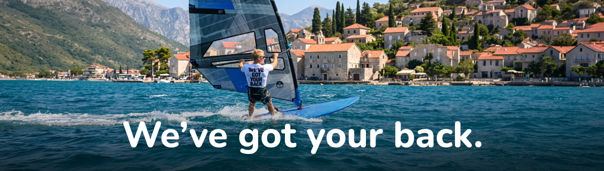 A windsurfer riding past a coastal town, wearing a We've got your back top.