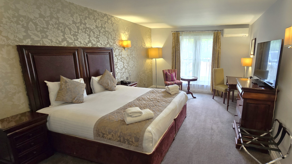 Spacious hotel bedroom at Shendish Manor with a king-size bed in white linens, bedside lamps, armchair and window.