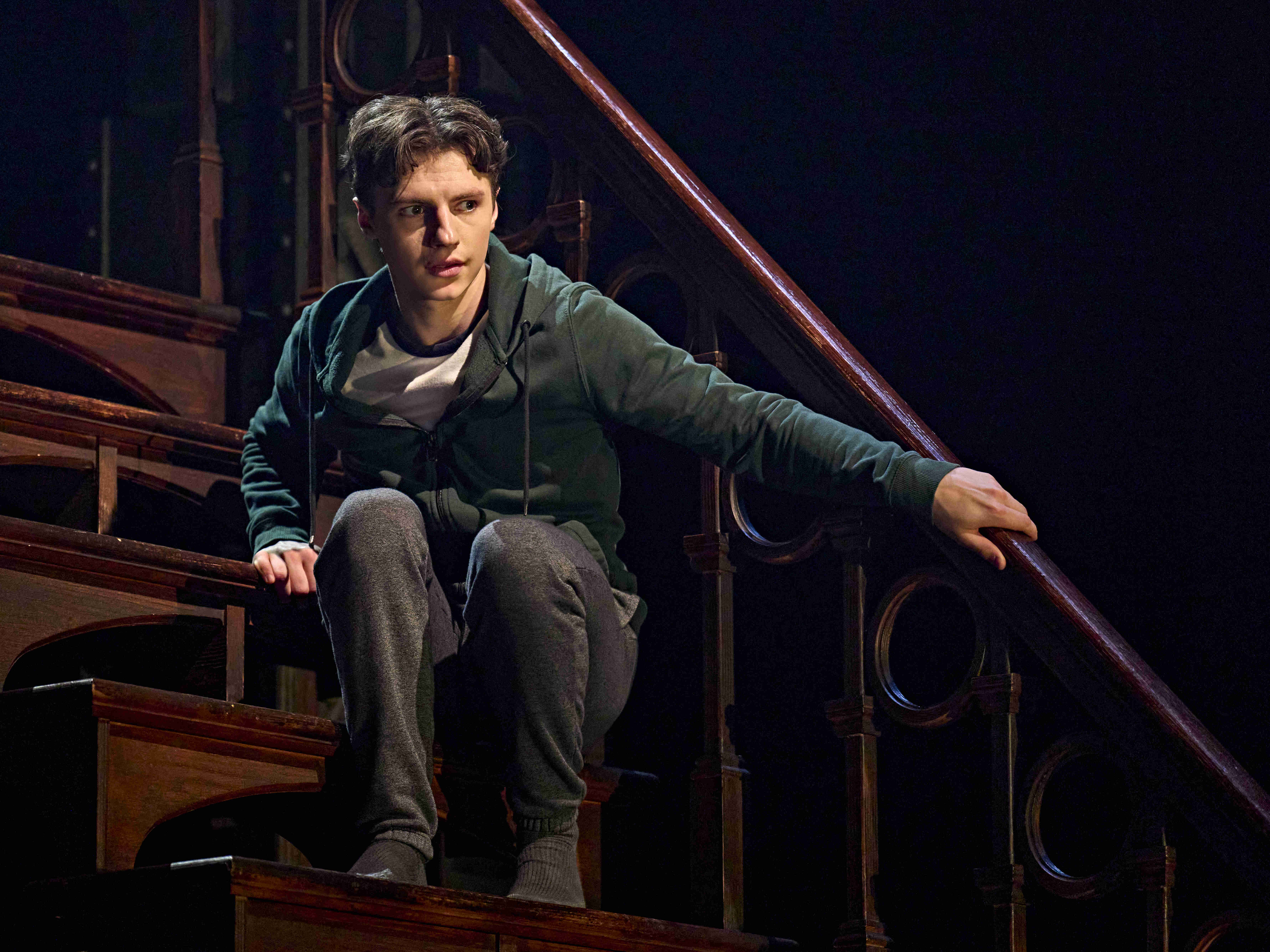 A giant character on the stairs reaching out to a man in pajamas with others looking on in awe, from Harry Potter and the Cursed Child.