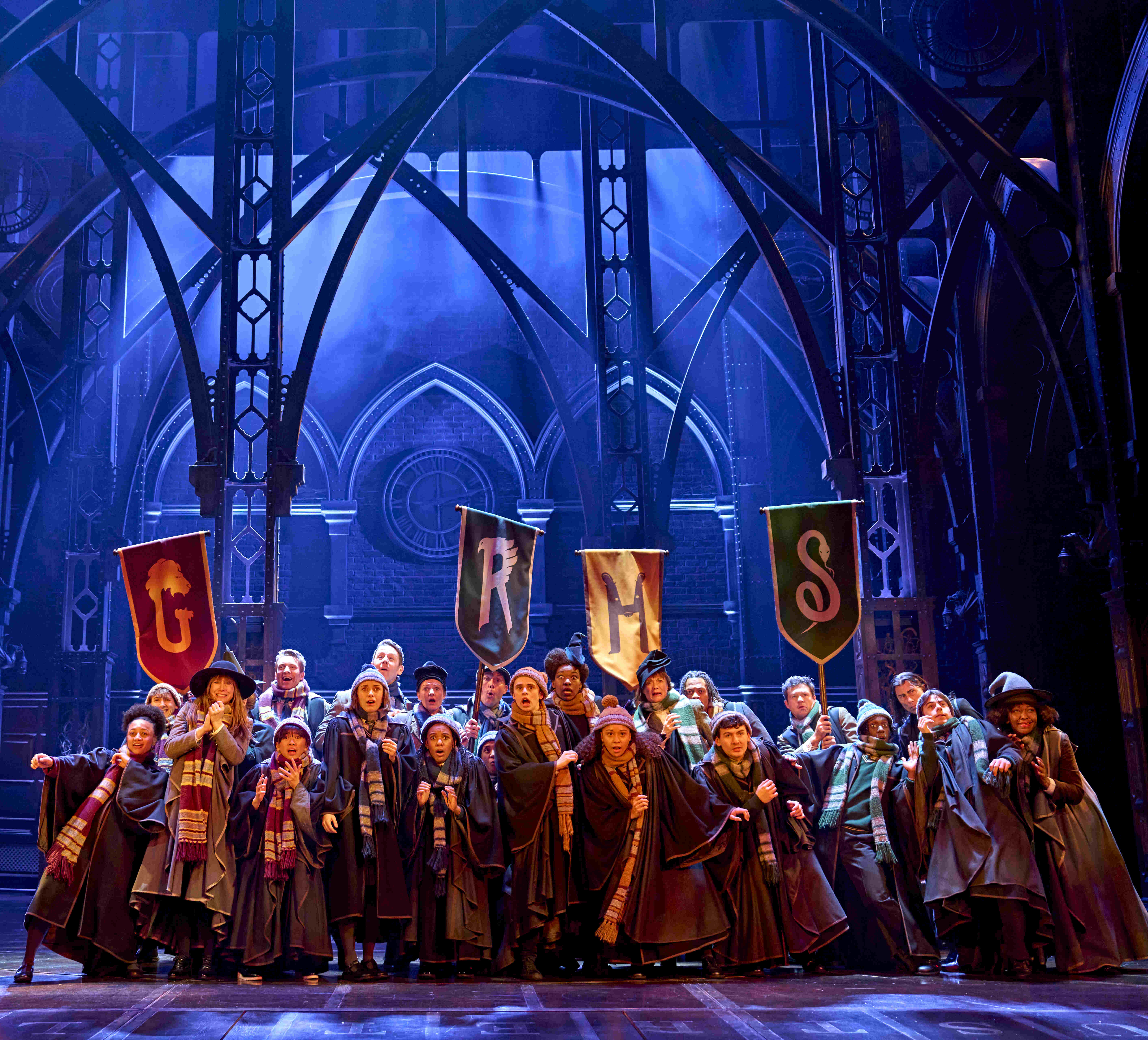 A character resembling Dumbledore raising a wand in a dramatic scene, illuminated in blue lighting, from Harry Potter and the Cursed Child.
