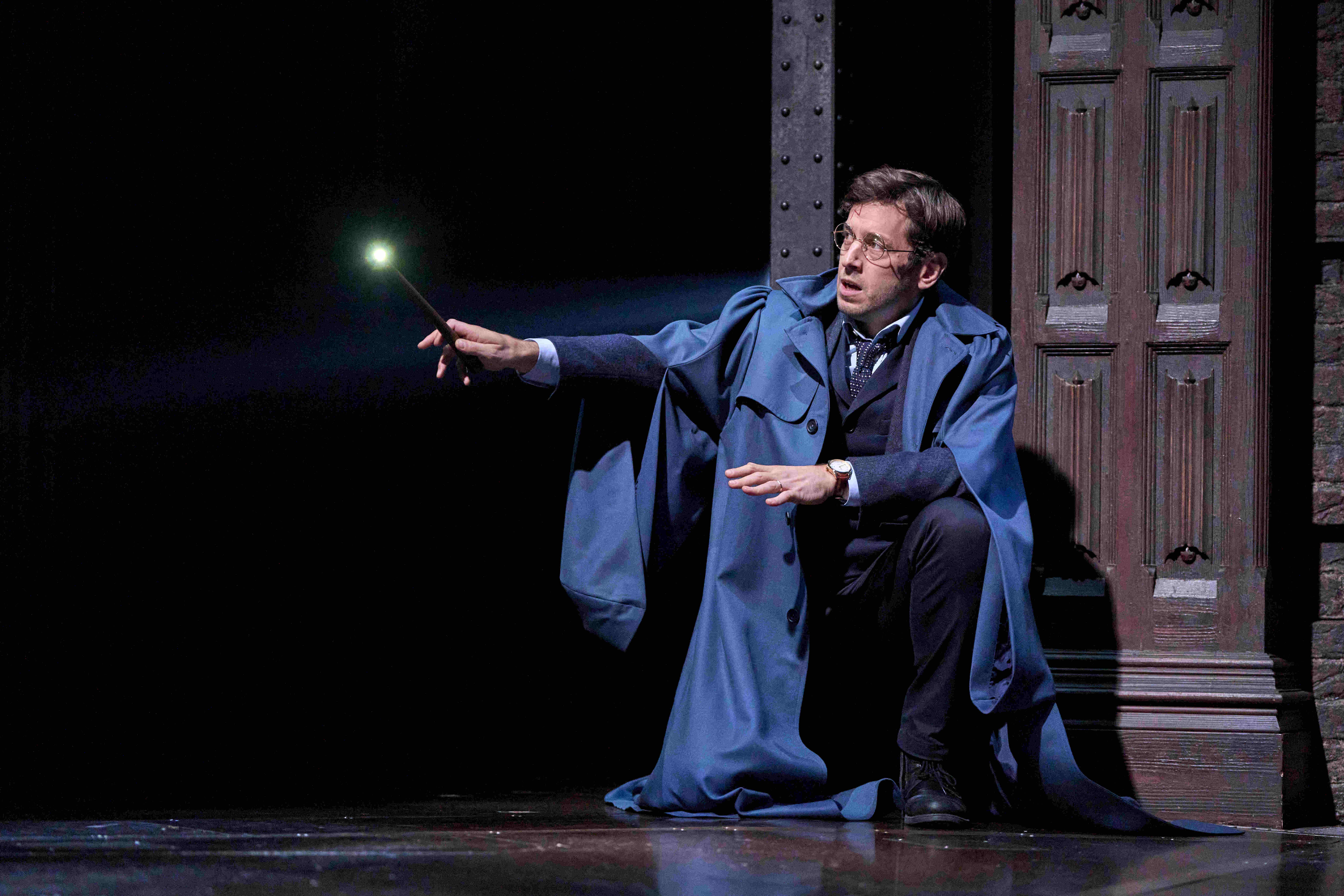 Character in blue coat casting a spell with a wand during a performance of Harry Potter and the Cursed Child.
