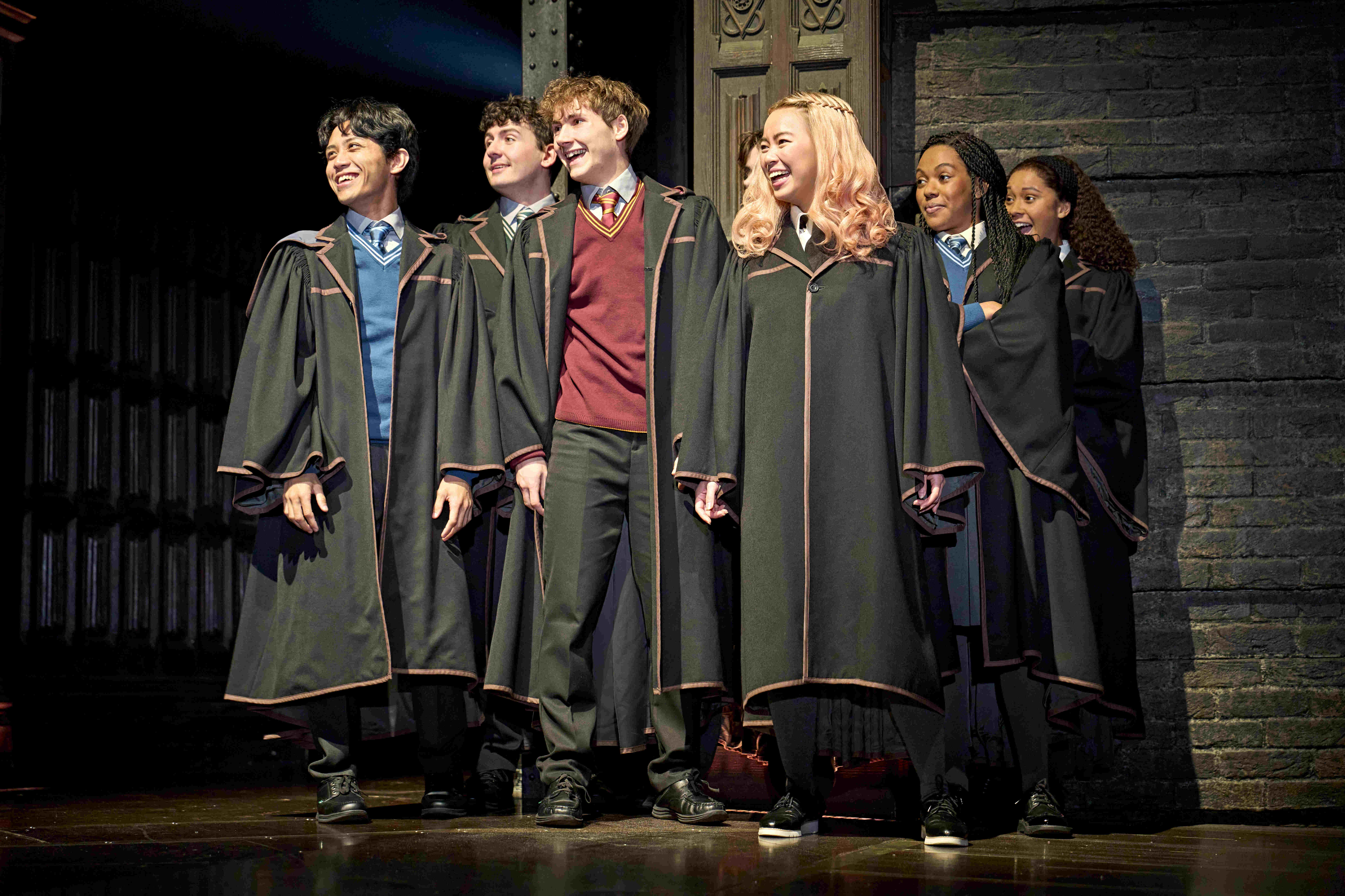 Gryffindor and Slytherin students sitting on trunks and waving in Harry Potter and the Cursed Child.
