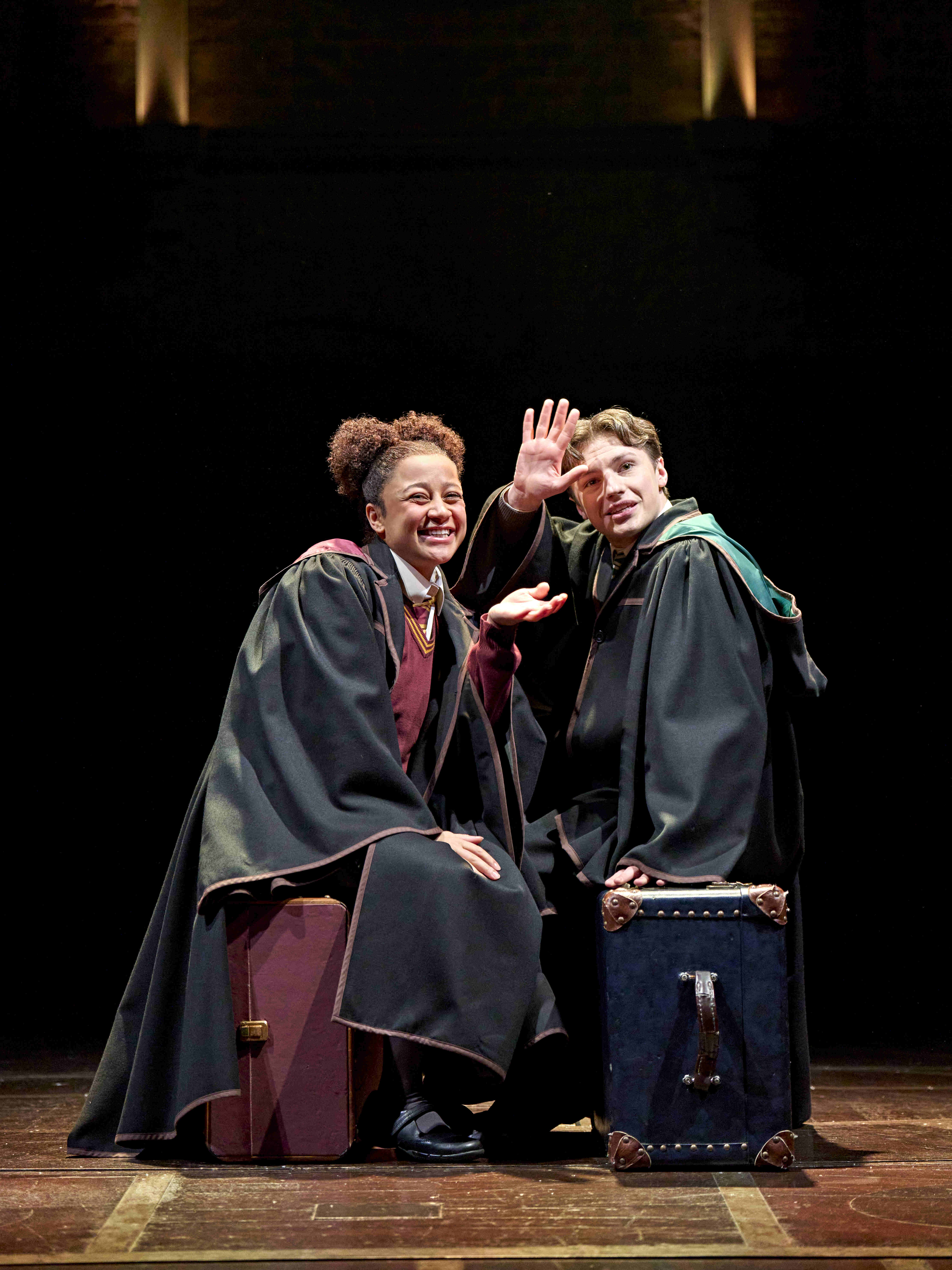Actor performing a magical scene, casting a spell with a wand, surrounded by Hogwarts house banners in Harry Potter and the Cursed Child.