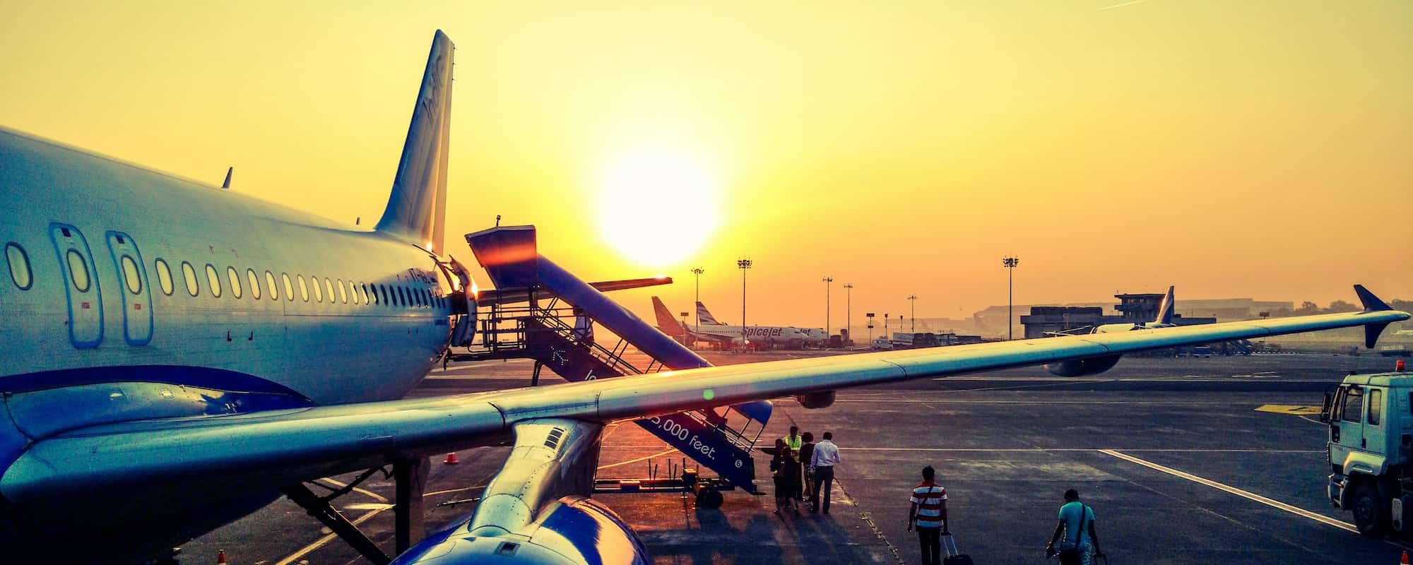 Image of holidaymakers boarding a plane while the sun sets in the background