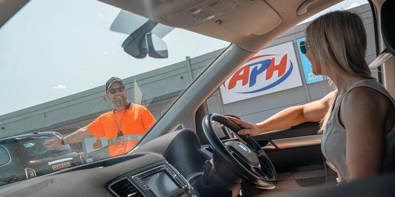 Driving up to an airport car park in front of a smiling staff member in an orange high-vis jacket