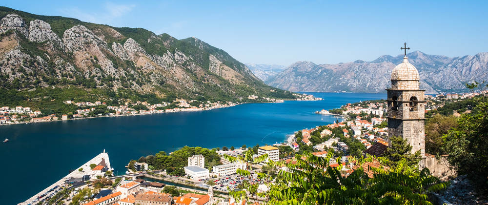 Panoramic Kotor Bay, Montenegro with turquoise Adriatic water, coastal town, steep mountains, and historic stone church tower – scenic travel view.