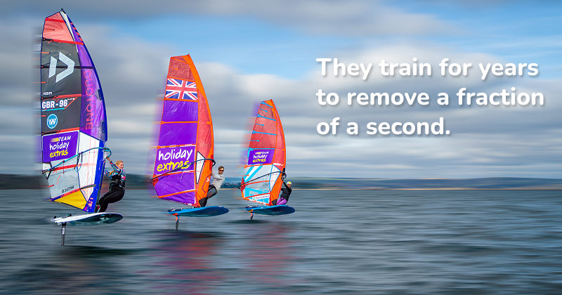 Three windsurfers racing on hydrofoil boards across open water, colorful sails raised, moving fast under a cloudy sky — competitive windsurfing action.