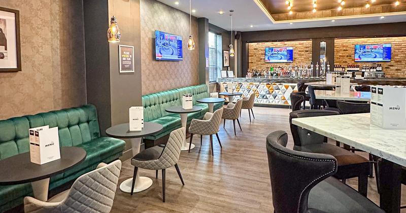 Shark Club Gastro Bar at Sandman Signature London Gatwick Hotel. Modern bar and restaurant interior with green booth seating, marble tables, upholstered chairs, wood flooring, and a stylish cocktail bar.