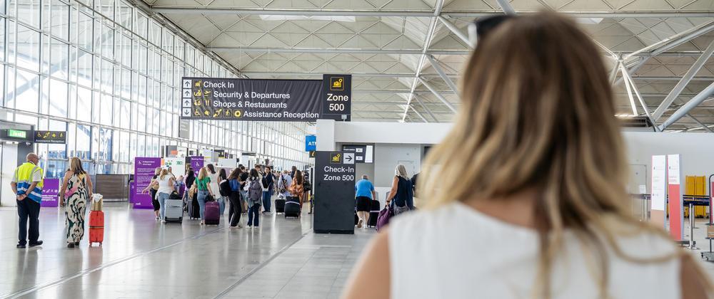 Traveller walking through Stansted Airport toward check-in and departures area with passengers, luggage, and overhead signs.
