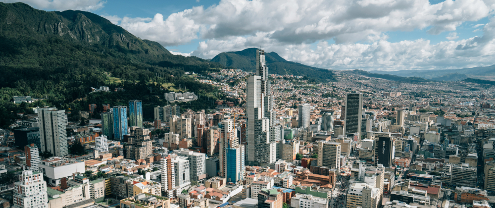 Aerial view of Bogotá skyline with modern skyscrapers, dense urban buildings, and green mountains under dramatic clouds – vibrant Colombian cityscape.