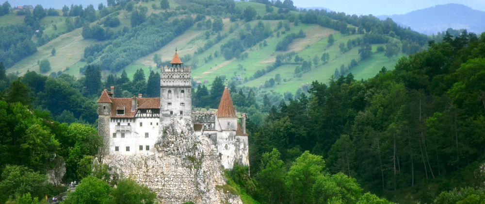 Bran Castle, historic medieval castle perched on a rocky hill, surrounded by dense forest and rolling green mountains – scenic European countryside landmark.