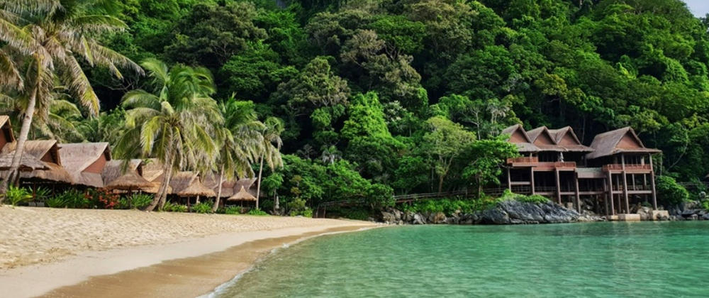 Tropical beach with palm trees and wooden beachfront villas beside clear turquoise water and lush green jungle – Cauayan Island Resort in El Nido, Palawan, Philippines.