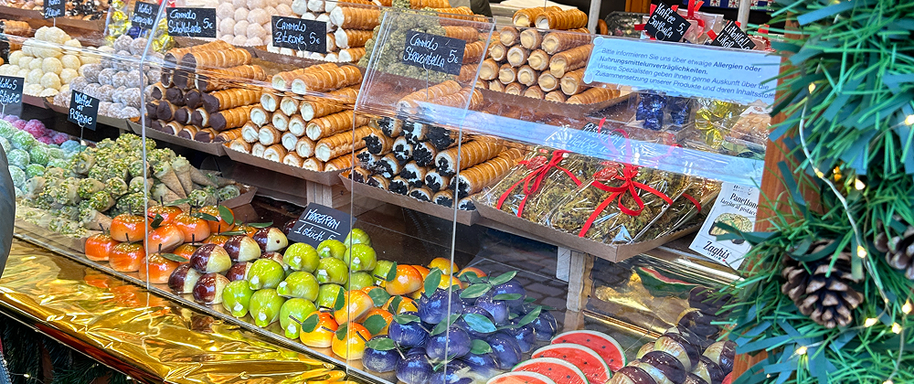 Close-up of marzipan fruits, cannoli, and colorful pastries in a Christmas market bakery display — festive European holiday sweets and desserts.