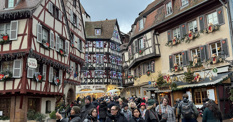 Colorful half-timbered houses decorated for Christmas in Colmar, France, with festive garlands, ornaments, and shuttered windows — charming holiday village.