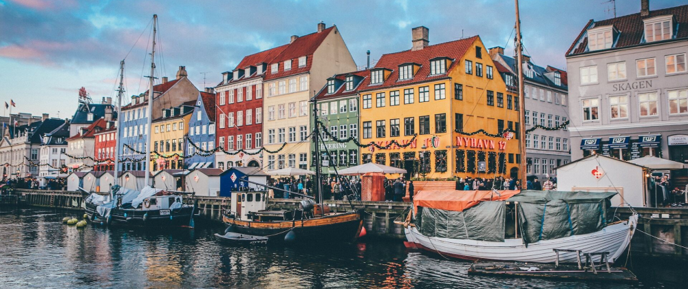 Colourful waterfront buildings along Nyhavn Canal in Copenhagen with moored boats, reflections on the water, and a lively historic harbour atmosphere.