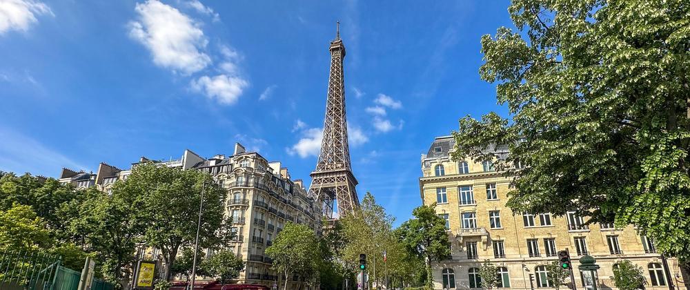 Eiffel Tower rising above classic Parisian buildings and green trees under a bright blue sky – scenic view of Paris architecture and landmark.