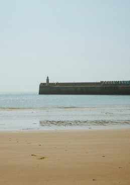 Sunny Sands Beach with Lighthouse Champagne Bar, Harbour Arm and Folkestone sign in the background.