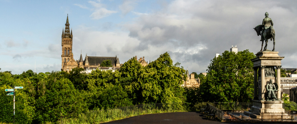 Equestrian statue in a green city park overlooking Glasgow skyline, with historic university tower, trees, and dramatic cloudy sky – iconic Scotland landmark.