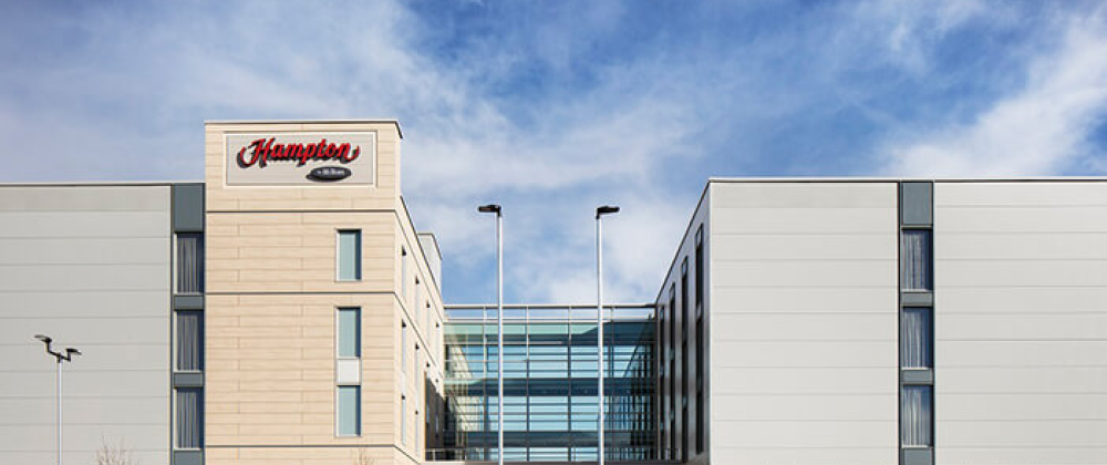 Hampton by Hilton Bristol Airport hotel building with modern architecture, glass central walkway, and blue sky background in a contemporary urban setting.