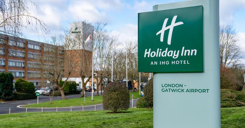 Holiday Inn London – Gatwick Airport sign in front of a modern brick hotel with trees, driveway, and green lawn — convenient airport hotel location.