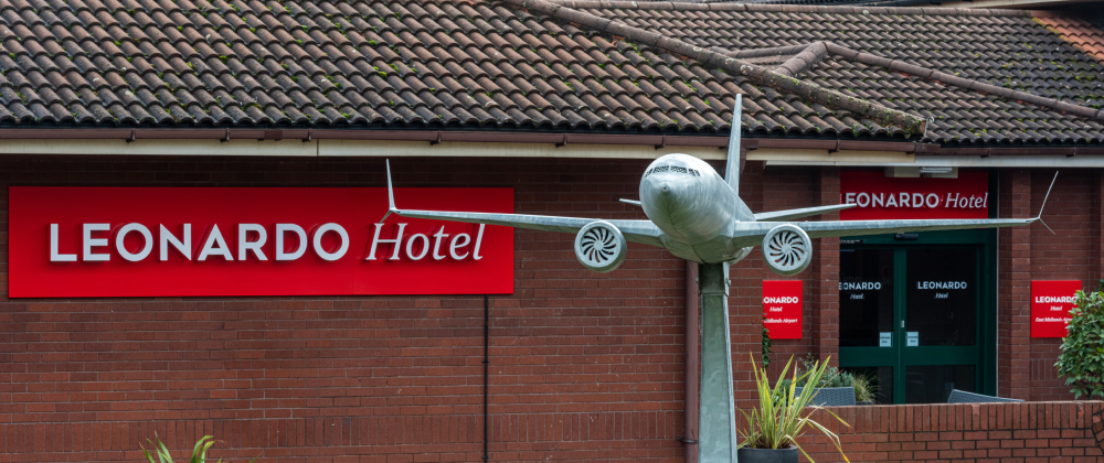 Leonardo Hotel East Midlands Airport entrance with large airplane sculpture mounted outside, red hotel signage, and brick building facade.