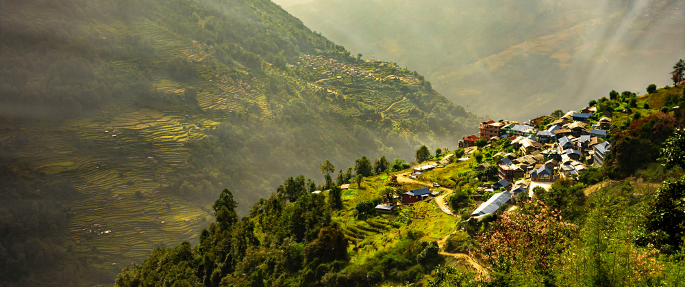Sunlit mountain village surrounded by lush green terraced fields and forested hills, with misty valleys and dramatic rays of sunlight – Nepal.