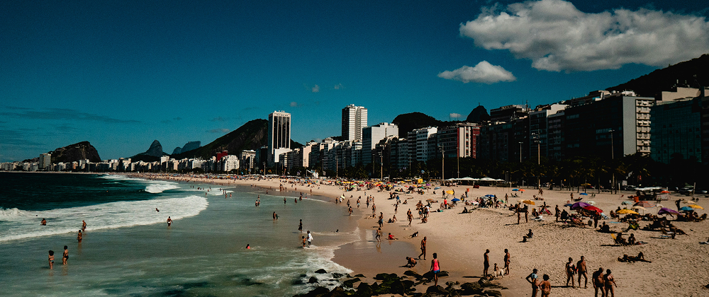 People relaxing and swimming on Copacabana Beach in Rio de Janeiro, Brazil with city skyline and mountains in the background — lively summer destination.