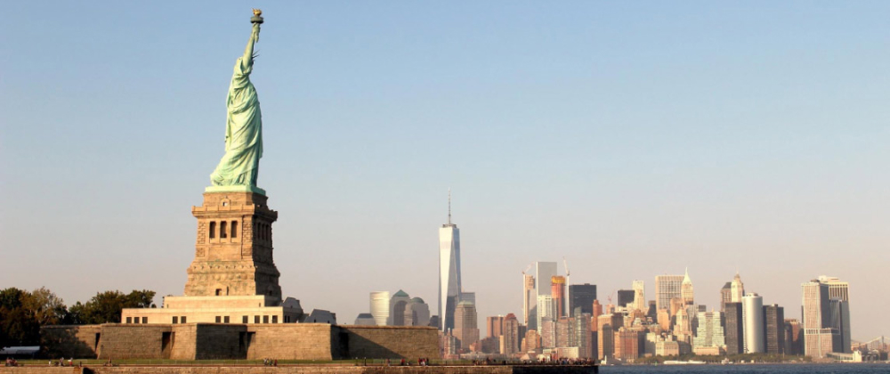 Statue of Liberty in front of the New York City skyline at sunset, with One World Trade Center rising among skyscrapers – iconic cityscape and landmark.
