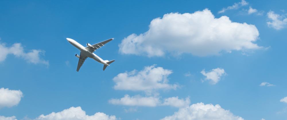 Commercial airplane flying through a bright blue sky with scattered white clouds – travel and aviation concept in clear weather.