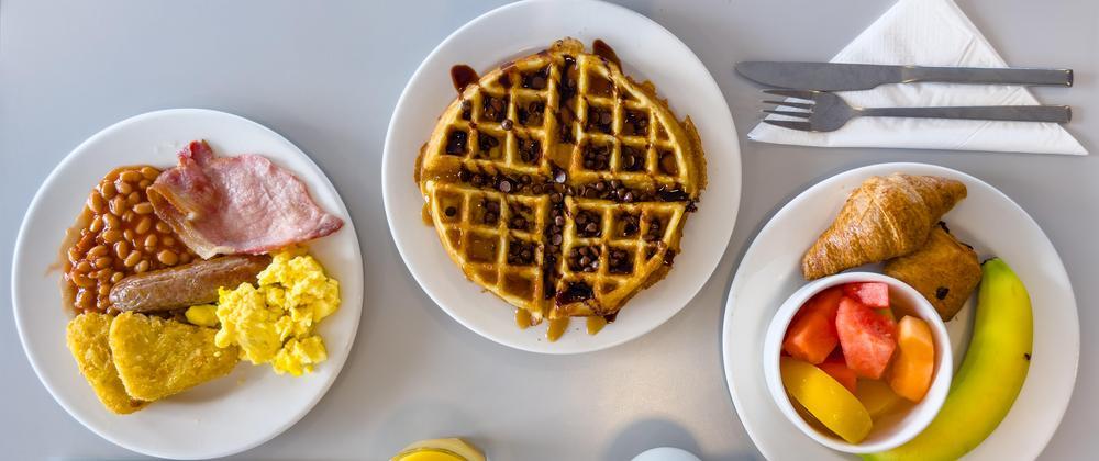 Full English breakfast, chocolate chip waffle with syrup, and fresh fruit with pastries at Hampton by Hilton Stansted Airport buffet.