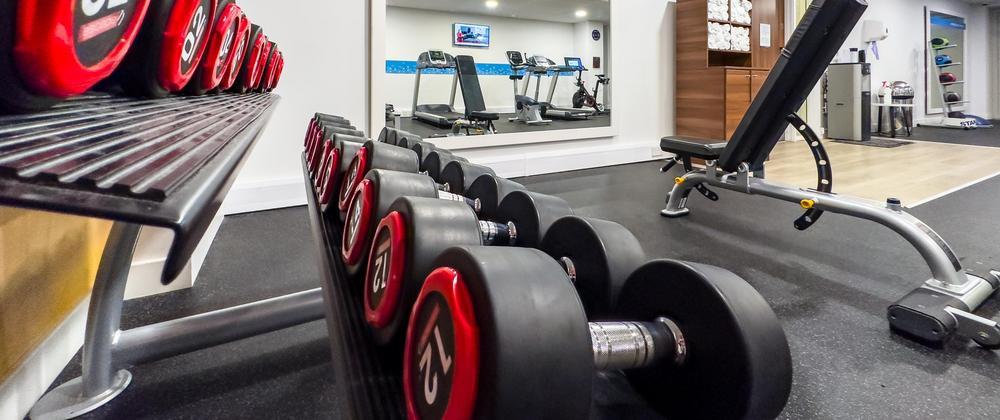 Fitness center at Hampton by Hilton Stansted with free weights, bench press, cardio machines, and towel station—modern gym for hotel guests.