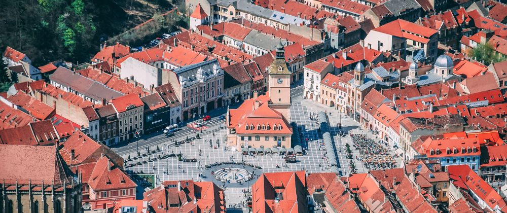 Aerial view of a historic city centre with red-roofed buildings surrounding a large public square and clock tower.
