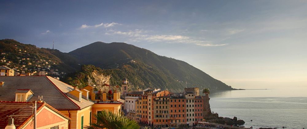 Colourful coastal buildings beside the sea with green mountains rising behind them.