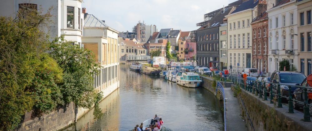 Canal lined with historic buildings, parked cars and small boats.