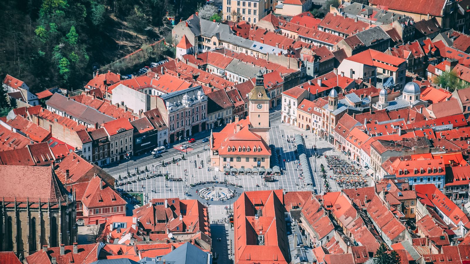 Aerial view of a historic city centre with red-roofed buildings surrounding a large public square and clock tower.