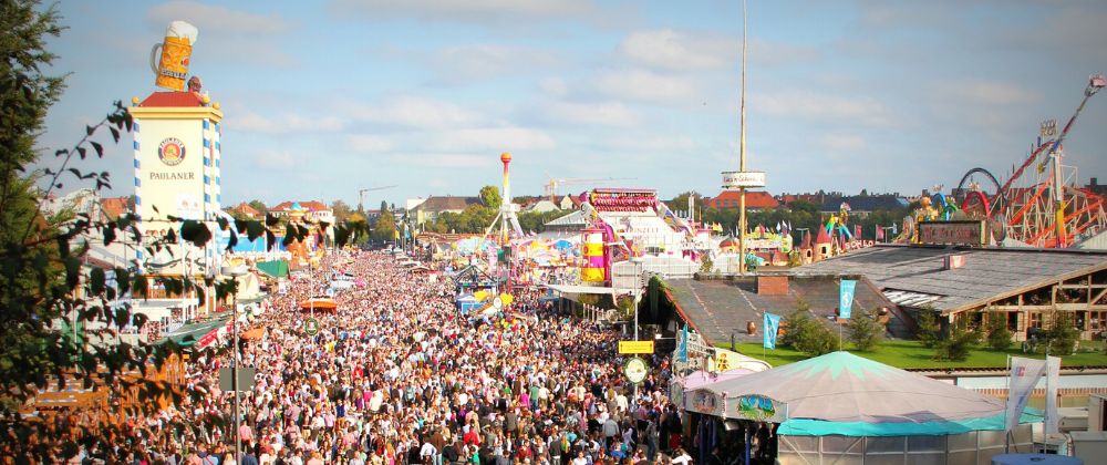 Large crowds filling a colourful outdoor fairground with rides, stalls and tents