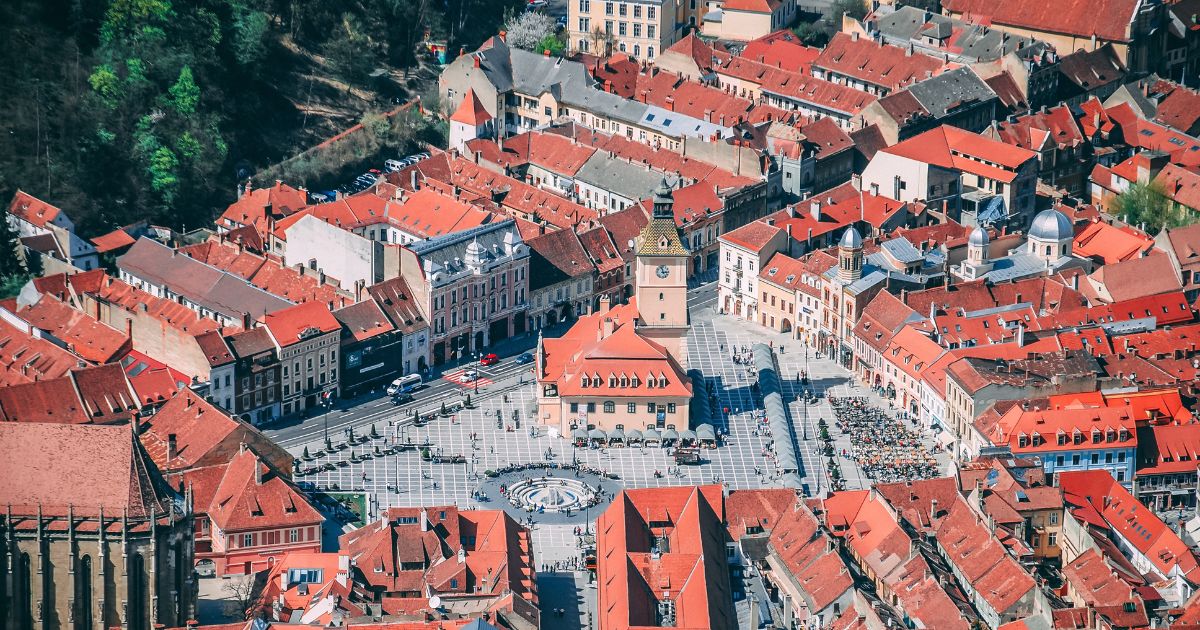 Aerial view of a historic city centre with red-roofed buildings surrounding a large public square and clock tower.