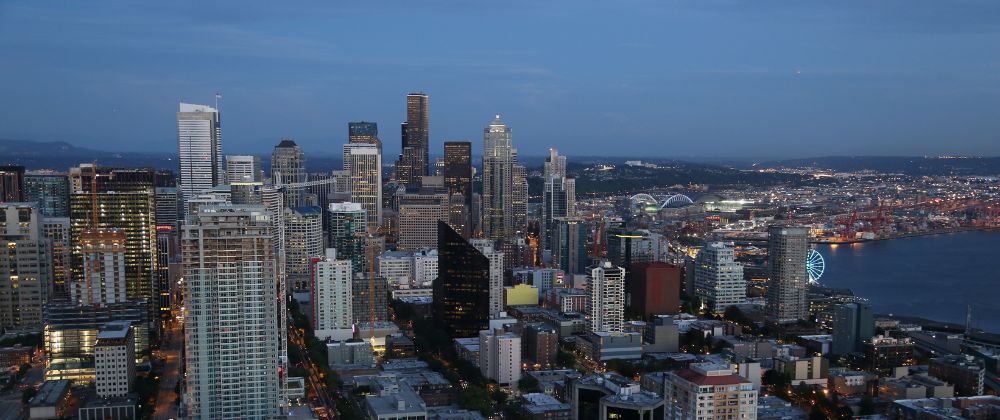 City skyline at dusk with high-rise buildings, a waterfront and illuminated Ferris wheel.