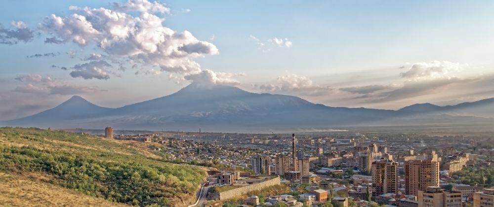 City spreading across a valley beneath a large mountain range at sunset.
