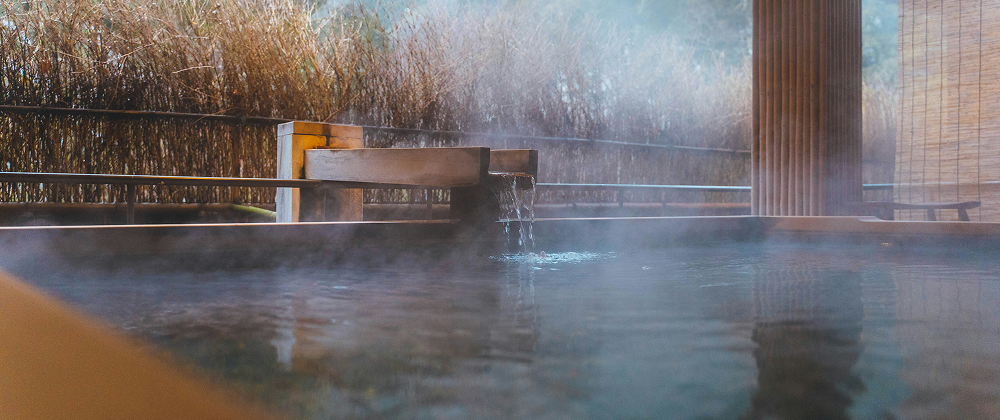 Steaming hot spring bath with wooden edges and a natural outdoor backdrop — relaxing Japanese onsen experience.