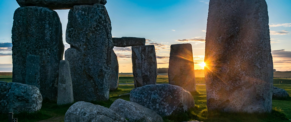 Sunrise at Stonehenge with sunlight beaming through ancient standing stones — iconic prehistoric site in England.
