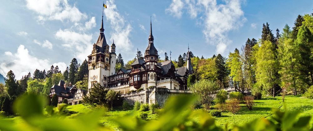 Pele? Castle in Romania surrounded by lush forest and green hills under a bright blue sky — fairytale architecture in the heart of Transylvania.