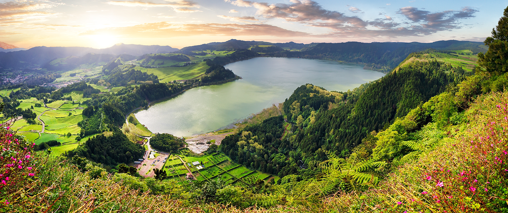 Lush green crater lake surrounded by hills and farmland at sunrise in the Azores — panoramic view of Sete Cidades, São Miguel Island.
