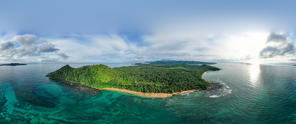 Drone view of lush tropical island surrounded by turquoise ocean and coral reefs — remote paradise with dense forest and beaches.
