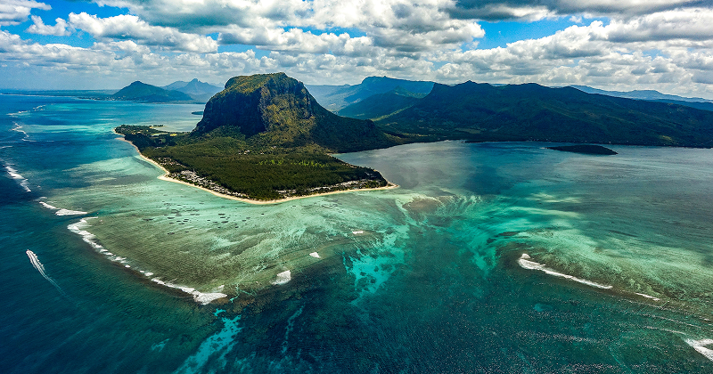 Aerial view of Le Morne Brabant mountain on Mauritius island, surrounded by turquoise lagoon, coral reefs, and lush greenery — tropical paradise landscape.