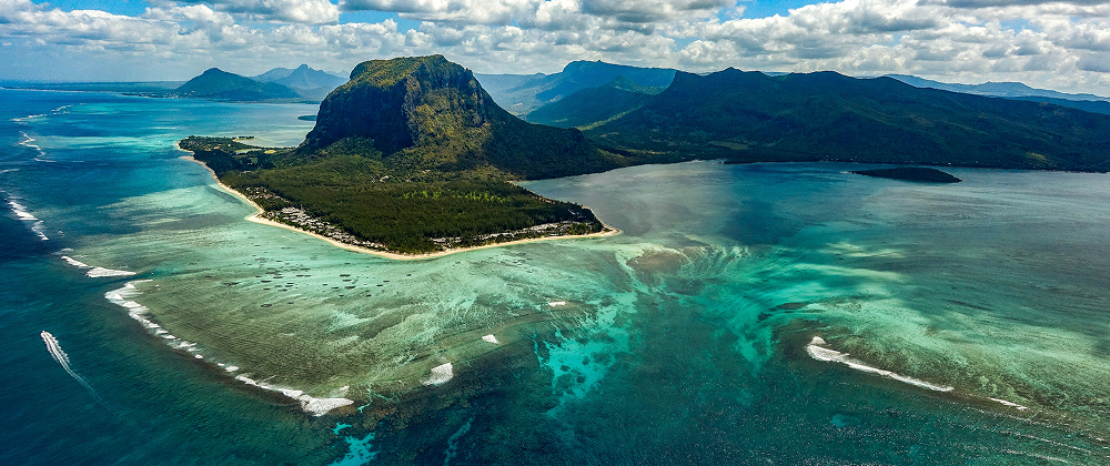 Aerial view of Le Morne Brabant mountain on Mauritius island, surrounded by turquoise lagoon, coral reefs, and lush greenery — tropical paradise landscape.