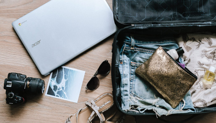 a suitcase with a makeup bag backed with a camera and laptop on the side