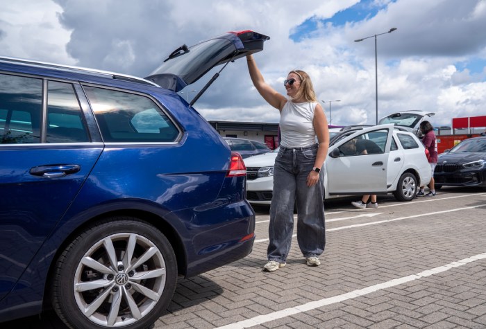 Smiling woman off loading travel luggage from the boot of her car at Holiday Extras Park & Ride at Gatwick Airport